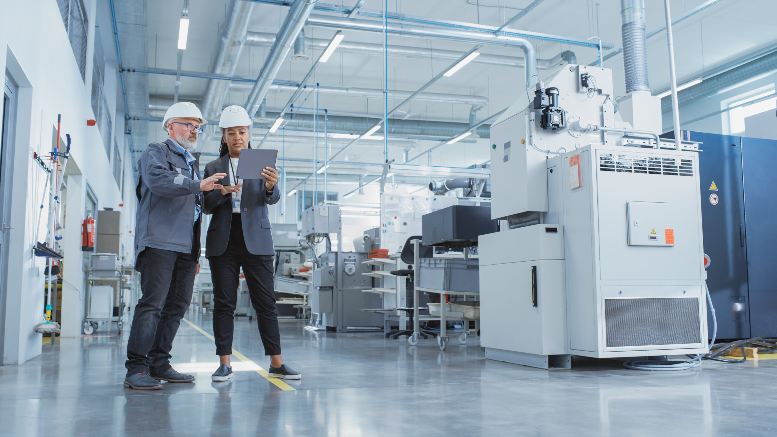 Portrait of Two Heavy Industry Employees in Hard Hats at Factory. Checking and Discussing Industrial Facility, Using Tablet Computer. African American Engineer and Middle Aged Technician at Work.